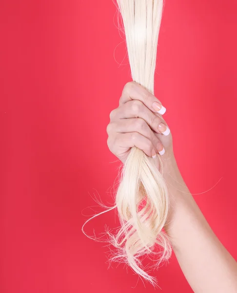 Cabelo loiro na mão feminina sobre fundo vermelho — Fotografia de Stock