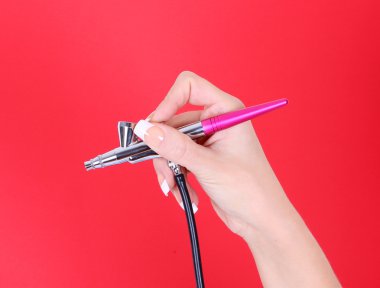 elinde kırmızı bir arka plan üzerinde kozmetik airbrush