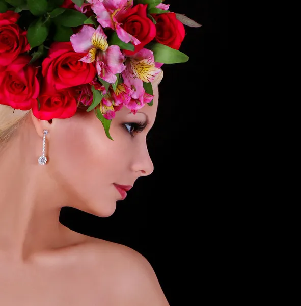 Modelo de moda com penteado com belas flores sobre fundo preto, jovem com rosas vermelhas e íris rosa em seu cabelo — Fotografia de Stock