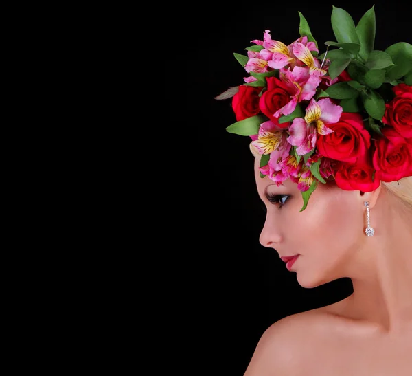 Modelka s účes s krásnými květinami černém pozadí, mladá žena s červenými růžemi a růžové kosatce ve vlasech — Stockfoto