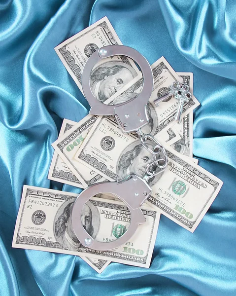 Money and handcuffs on turquoise silk fabric, dollars bills — Stock Photo, Image