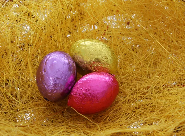 Uova di Pasqua, tre colorate uova di cioccolato lucido sopra paglia — Foto Stock