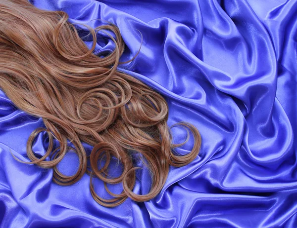 Krullend bruin haar op blauwe zijde textiel — Stockfoto