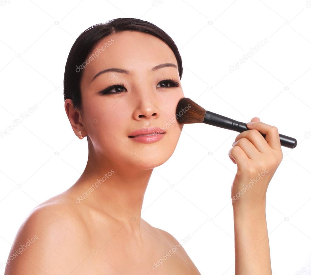 Woman with makeup brush. beautiful Asian brunette applying blush on her cheek, isolated on white