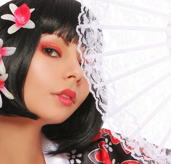 Geisha with lace fan and beautiful flowers in her black hair, over white background. sexy brunette — Stock Photo, Image