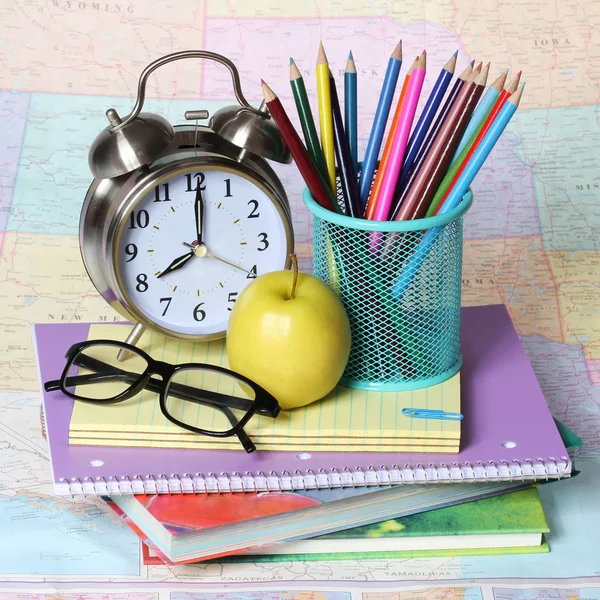 Terug naar school concept. een appel, gekleurde potloden, bril en wekker op stapel boeken over de kaart — Stockfoto