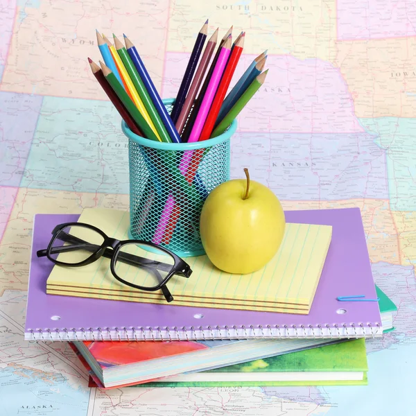 Terug naar school concept. een appel, gekleurde potloden en bril op stapel boeken over kaart — Stockfoto