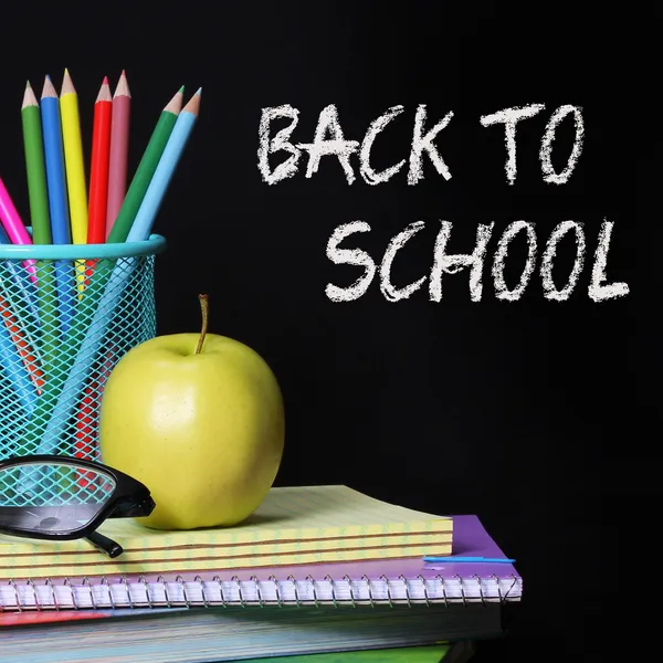 Back to school concept. An apple, colored pencils and glasses on pile of books over black background . The words 'Back to School' written in chalk on the blackboard — Stock Photo, Image