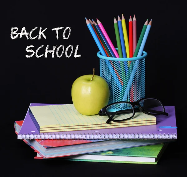 Vissza ehhez: iskola fogalmát. egy almát, színes ceruzák és a szemüveg a halom könyvet több mint a fekete háttér. a szavak "vissza az iskolába" krétával írt a táblára — Stock Fotó