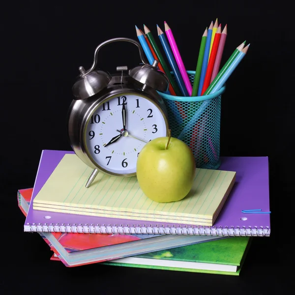 Torniamo al concetto di scuola. Una mela, matite colorate e sveglia su mucchio di libri su sfondo nero — Foto Stock