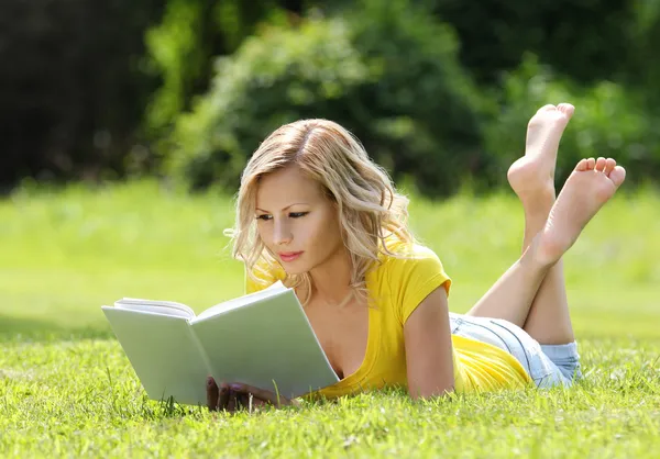 Flicka som läser boken. blond vacker ung kvinna med bok liggande i gräset. utomhus. solig dag. tillbaka till skolan — Stockfoto