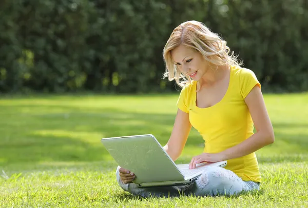 Ragazza con computer portatile. Bionda bella giovane donna con notebook seduto sull'erba. All'aperto. Giornata di sole. Ritorno a scuola — Foto Stock