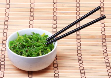 Susam bambu hasır üzerinde seramik kase yemek çubukları ile deniz yosunu. chuka salata. Japon mutfağı