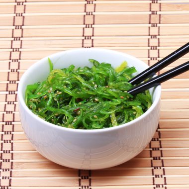 Susam bambu hasır üzerinde seramik kase yemek çubukları ile deniz yosunu. chuka salata. Japon mutfağı