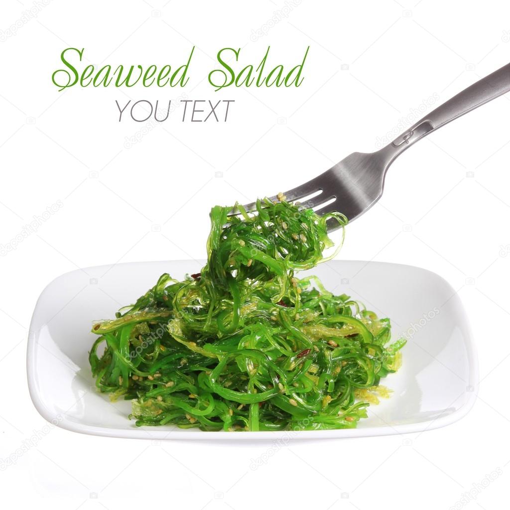 Chuka salad. Seaweed with sesame seeds on fork and ceramic plate, isolated on white background. Japanese Cuisine