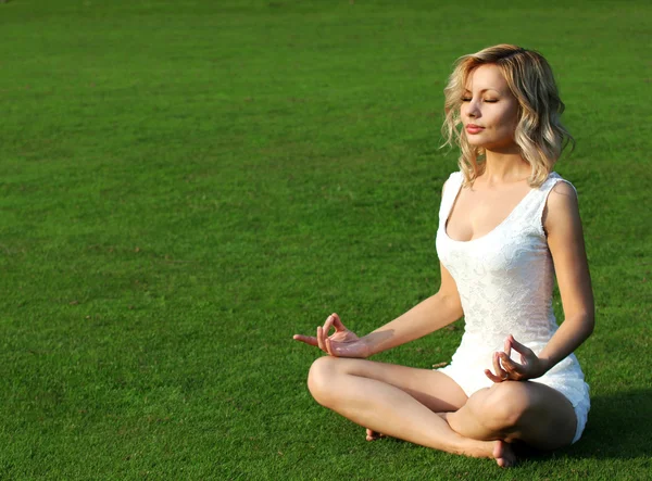 Sarışın kız yeşil çimenlerin üzerinde meditasyon. güzel genç kadın yoga poz Lotus Park oturma. açık havada — Stok fotoğraf