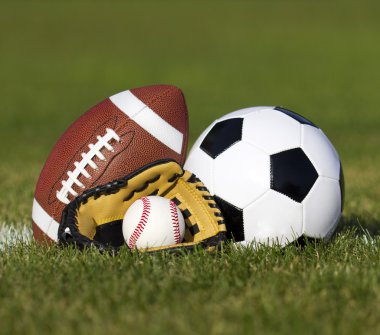 Sports balls on the field with yard line. Soccer ball, American football and Baseball in yellow glove on green grass. Outdoors clipart