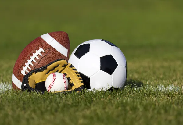 体育球在字段与码线上。足球球、 美式橄榄球和棒球在绿色草地上的黄色手套。户外活动 — 图库照片