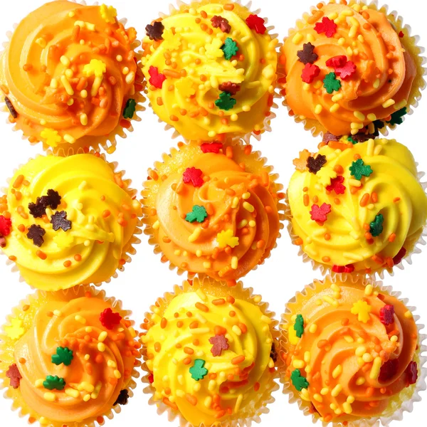 Muffins med gula och orange glasyr och färgade strössel. bakgrund. söt mat för halloween — Stockfoto