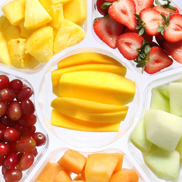 Piezas frescas de frutas en un recipiente de plástico. Comida saludable. Diferentes tipos de frutas en rodajas: mango, fresas, melón, uvas, piña . —  Fotos de Stock