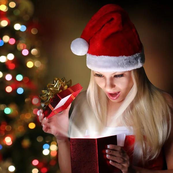 Navidad. Feliz chica rubia con Santa Sombrero apertura caja de regalo ove — Foto de Stock