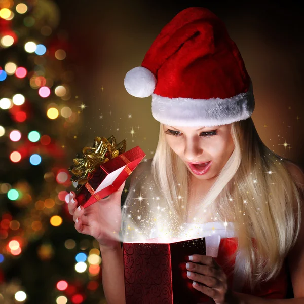 Різдво. Щаслива дівчина блондинка з Санта-Капелюхом відкриває подарункову коробку — стокове фото