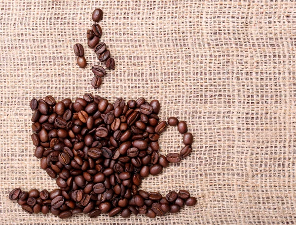 Granos de café, colocados en forma de taza en el fondo de lino o arpillera — Foto de Stock