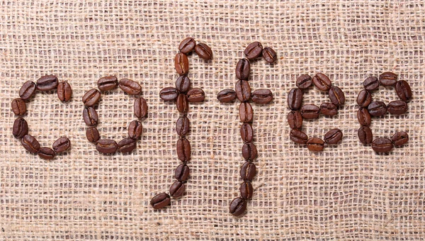 The word coffee made from coffee beans on burlap background — Stock Photo, Image