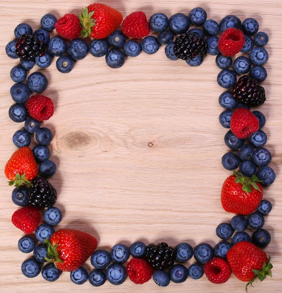 Beeren rahmen auf Holzgrund ein. Erdbeeren, Blaubeeren, Himbeeren und Brombeeren. — Stockfoto