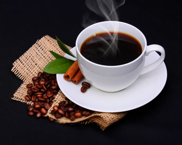 Tasse à café avec soucoupe et grains de café sur toile de jute sur noir — Photo