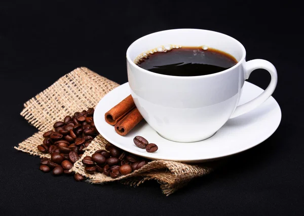 Coffee cup with saucer and coffee beans on burlap over black — Stock Photo, Image