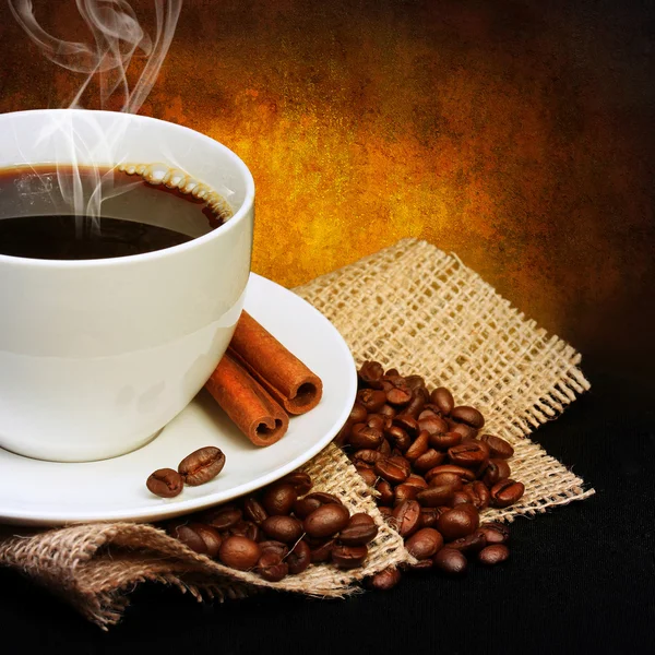 Kaffekopp med fat och kaffe bönor på säckväv över mörka rygg — Stockfoto