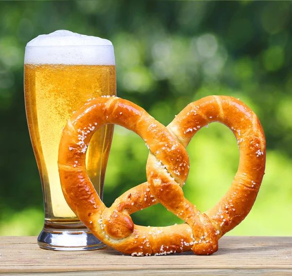 Ølglass med tysk Pretzel på trebord over naturgrønt – stockfoto