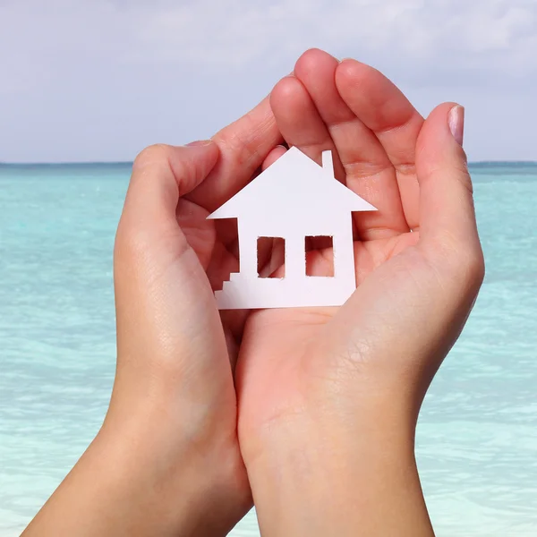 Χαρτί σπίτι στο θηλυκό χέρια πάνω από την τροπική παραλία. έννοια — Φωτογραφία Αρχείου
