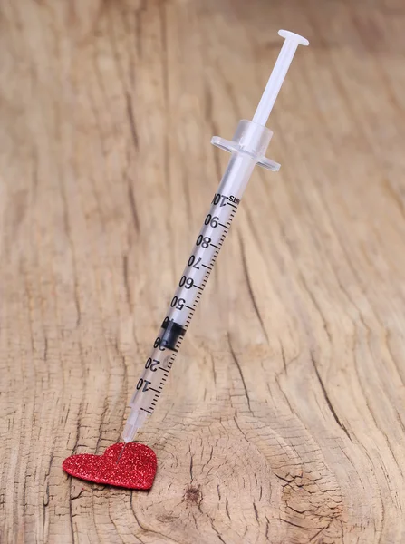 Glitter red heart and syringe with drug over wooden background. — Stock Photo, Image