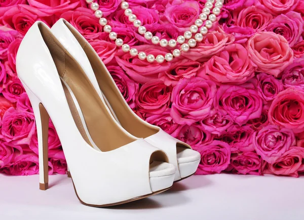 Bruids schoenen en rozen. witte hakken over hete roze bloemen — Stockfoto
