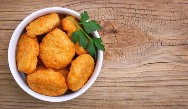 Chicken nuggets in bowl on wooden background — Stock Photo, Image