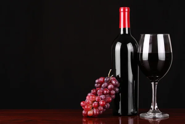 Weinflasche und Glas Rotwein mit frischen Trauben über schwarz — Stockfoto