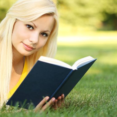 Yeşil çimenlerin üzerinde kitap ile sarışın kız. güzel bir kadın açık