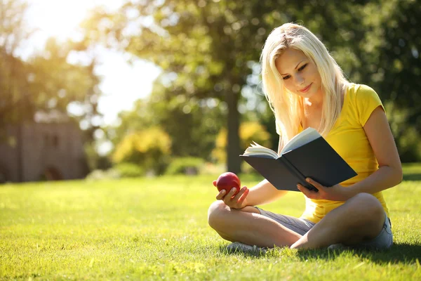 Blondynka z książki i jabłko na zielonej trawie. piękna kobieta — Zdjęcie stockowe