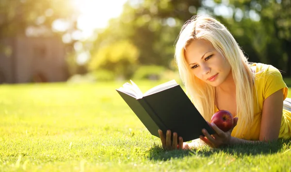 Blonde Girl with Book and Apple on Green Grass. Beautiful Woman Royalty Free Stock Photos