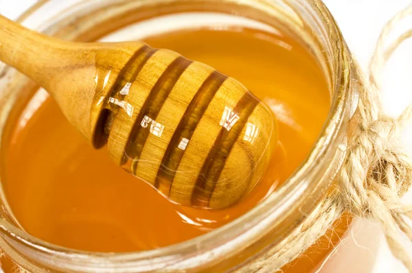 Glass jar with honey and wooden spoon — Stock Photo, Image