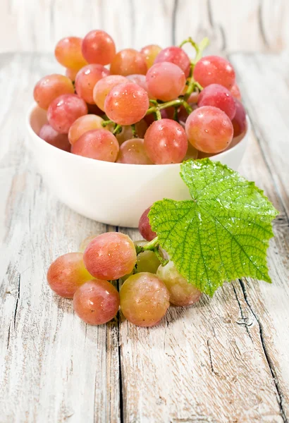 Uvas maduras em uma tigela branca com uma folha — Fotografia de Stock