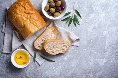 Yağla karışık lezzetli zeytinlerin üst görüntüsü ve gri beton zemin üzerinde ekmek dilimleri
