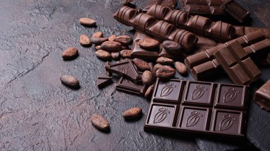 Kırık lezzetli süt parçaları ve kahverengi beton arka planda kakao çekirdekli siyah çikolata.