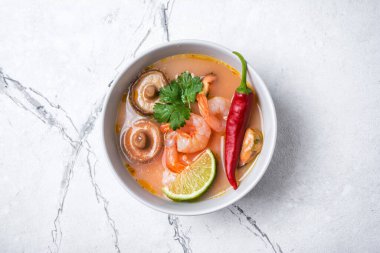 Tom Yam domates çorbası, lezzetli karidesler, midyeler, şiitake mantarları, kireç, beyaz mermer zemin üzerinde kırmızı biber