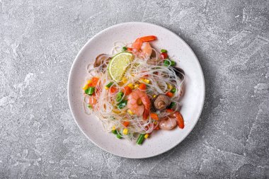 Japon fasulyeli veya cam erişteli tabağın üst görüntüsü, lezzetli karidesler, şitake mantarları ve gri beton arka planda sebzeler.