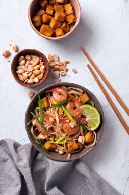 Asya usulü erişte, baharatlı karides, kızarmış tofu peyniri, fıstık, limon ve yeşil soğanlı beyaz mermer zemin.