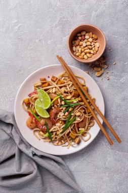 Asyalı udon eriştesi, baharatlı karides, kızarmış tofu peyniri, fıstık, limon ve yeşil soğanlı gri beton arka plan.