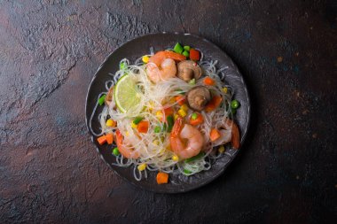 Japon fasulyeli veya cam erişteli tabağın üst görüntüsü, lezzetli karidesler, şitake mantarları ve kahverengi beton arka planda sebzeler.